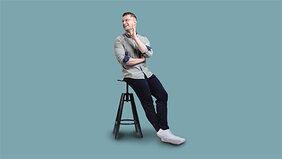 Junger Mann sitzt in dynamischer Pose auf einem Hocker